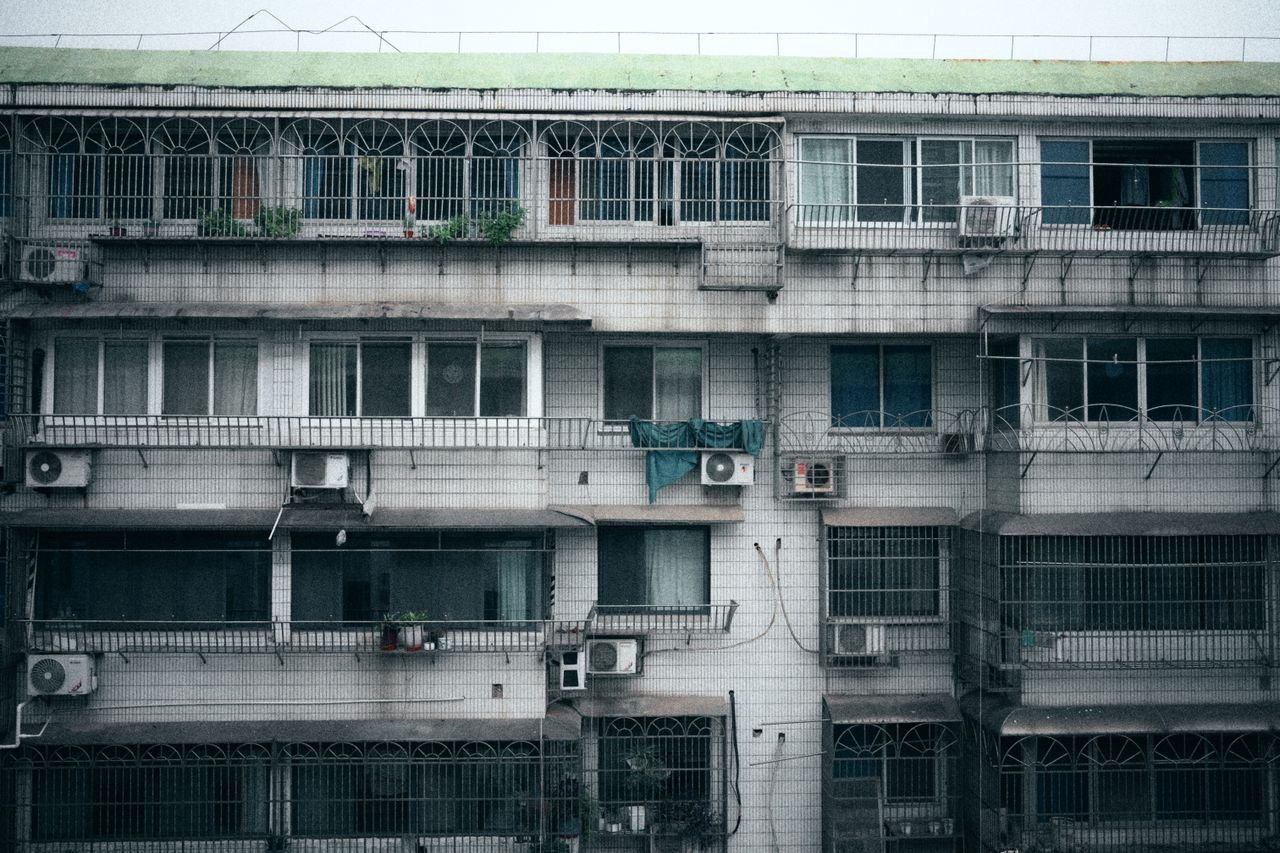 hero-img-01 Facade of a multi-story apartment building with air conditioning units visible on each floor.