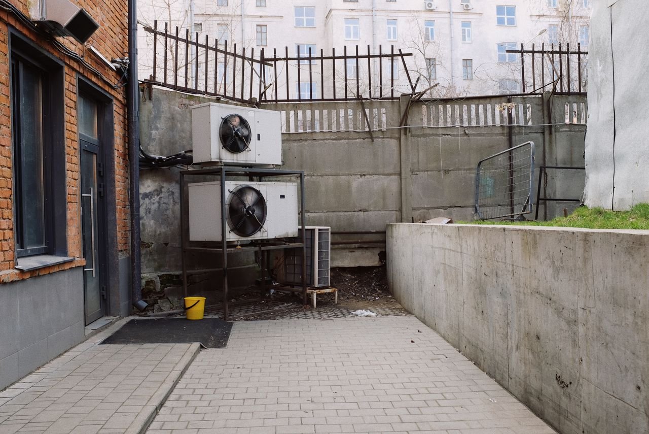our-services-1 Air conditioning system located outside concrete shabby fence with metal barrier near industrial building from bricks and glass door